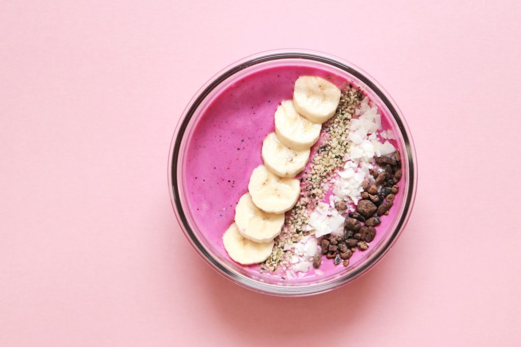 Pink smoothie in a bowl with banana slices and nuts