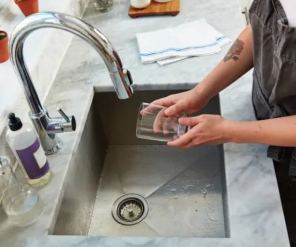 Someone holding a glass around the kitchen sink.