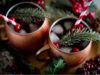 Two copper cups of cranberries sangria with a straw and rosemary in each cup.