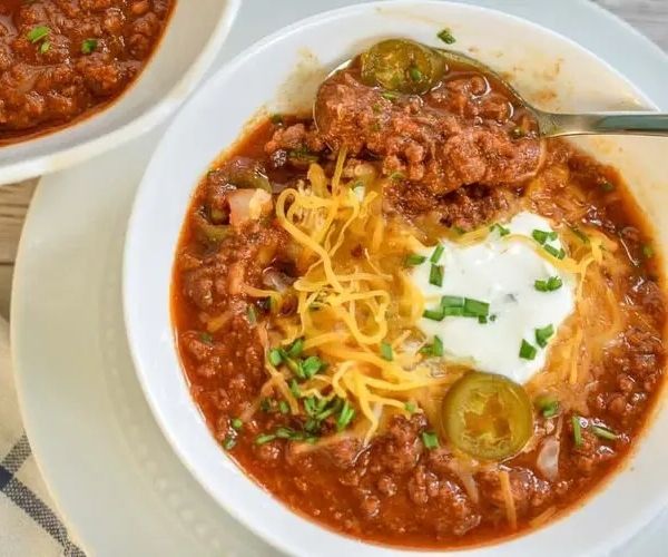 Chili soup with shredded cheese over and a spoon on a white bowl