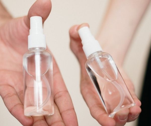 Two person holding two clear glass bottle spray